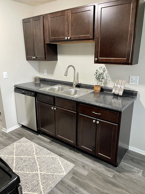 A kitchen with dark brown cabinets and a black dishwasher.