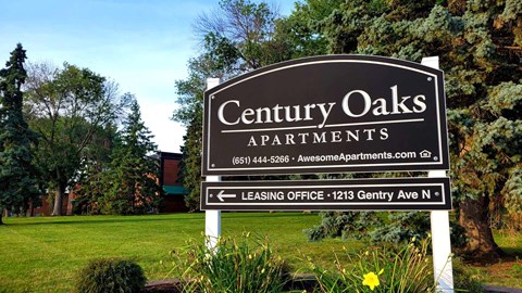 A sign for Century Oaks Apartments stands in front of a green lawn.