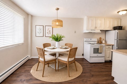A dining room with a table set for two and a kitchen area with white appliances.