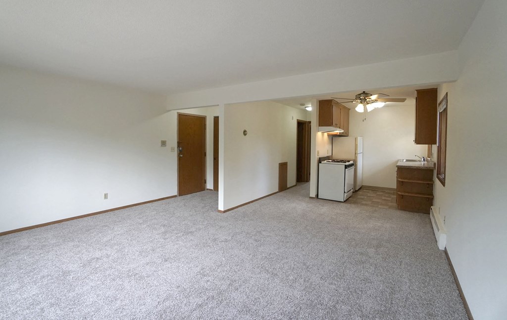 an empty living room with a kitchen in the background