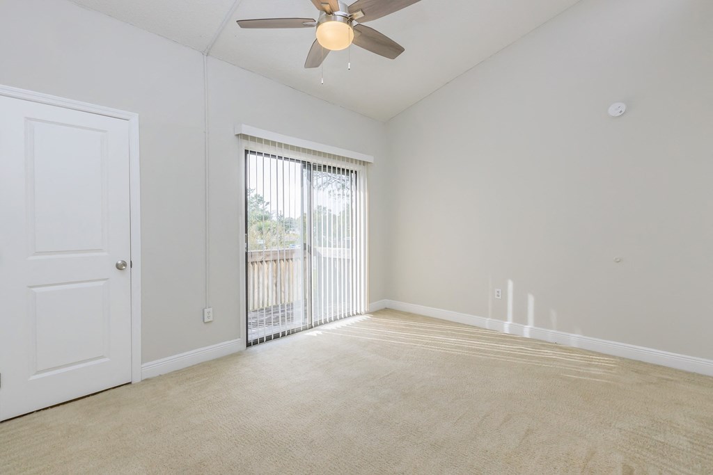 an empty living room with a ceiling fan and a door to a balcony