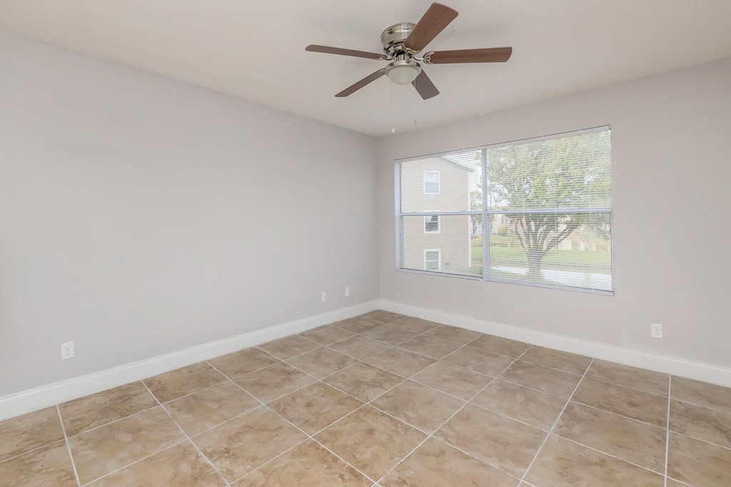 an empty living room with a large window and a ceiling fan