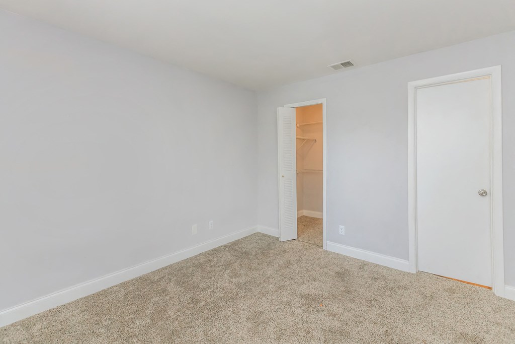 a bedroom with white walls and carpet and a closet