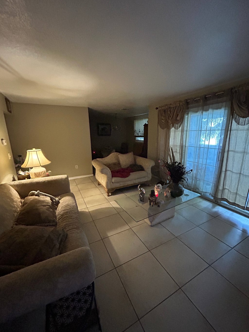 A living room with a couch, a chair, a lamp, and a table with a vase of flowers.