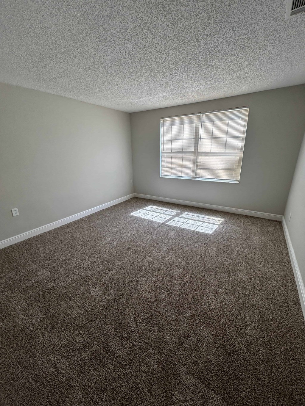 A room with a carpeted floor and a window with blinds.
