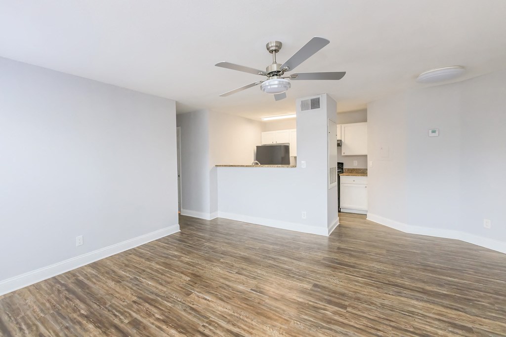 an empty living room with a ceiling fan and a kitchen