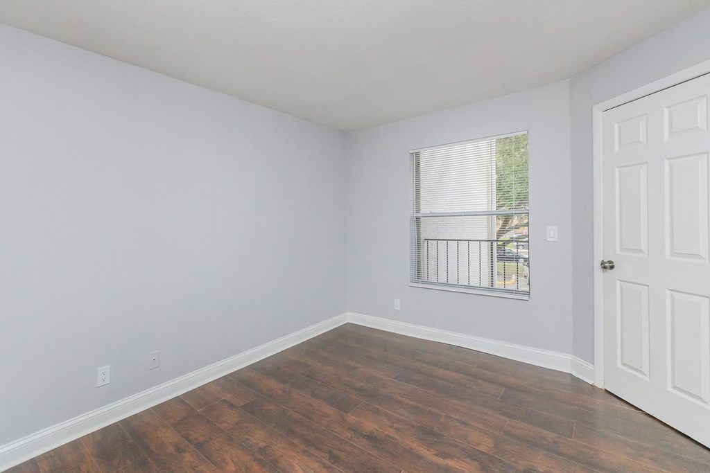 an empty bedroom with wood flooring and a window