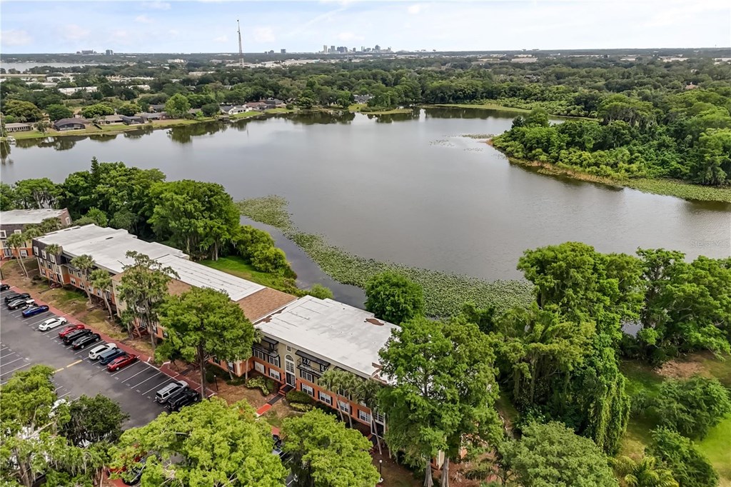 A large body of water surrounded by trees and a building with a parking lot in front.