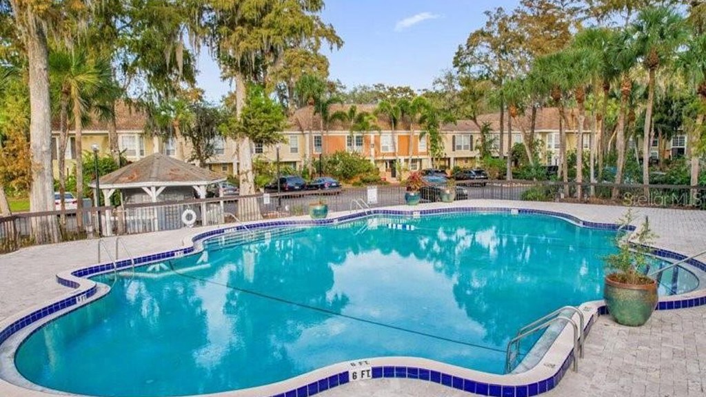 A large swimming pool surrounded by a brick border with a gazebo in the background.