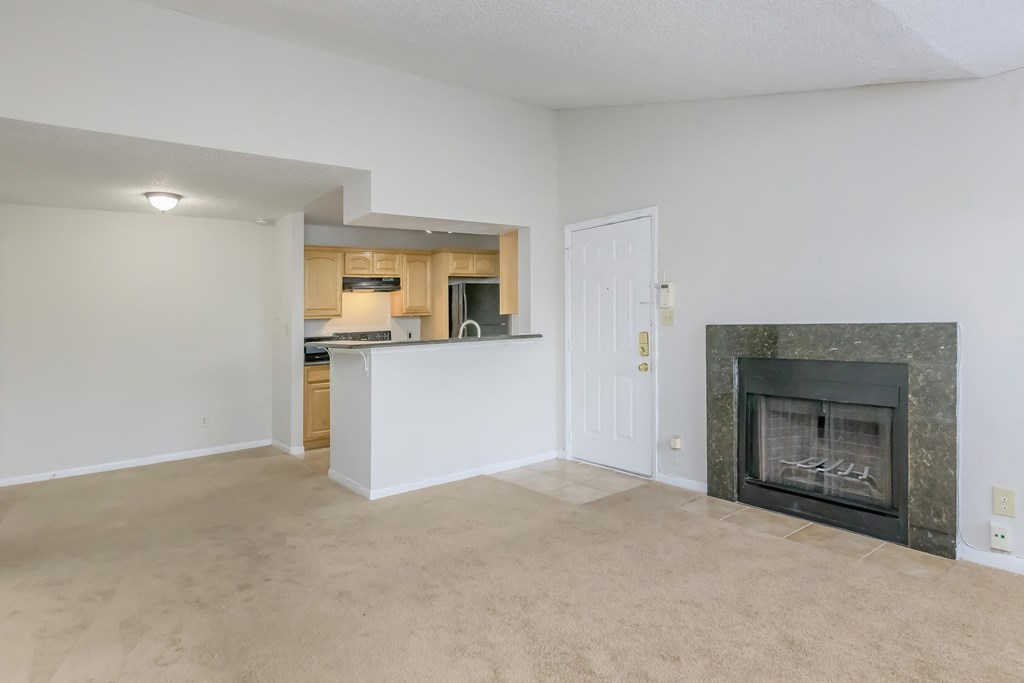 an empty living room with a fireplace and a kitchen