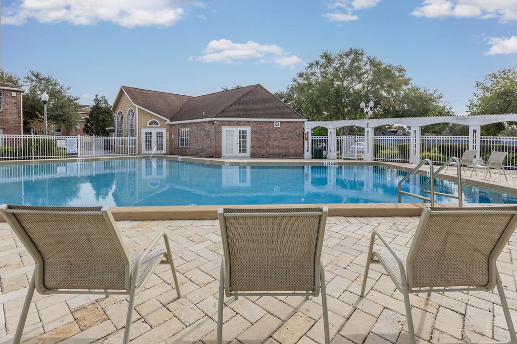 a swimming pool with chairs and a house in the background