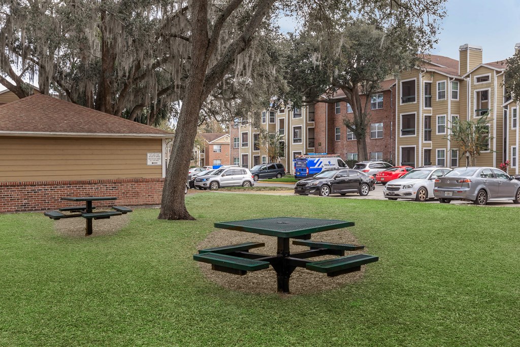 a park with picnic tables and cars in front of an apartment building