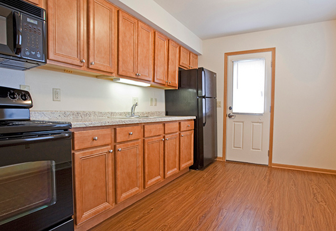 an empty kitchen with wooden cabinets and a black refrigerator