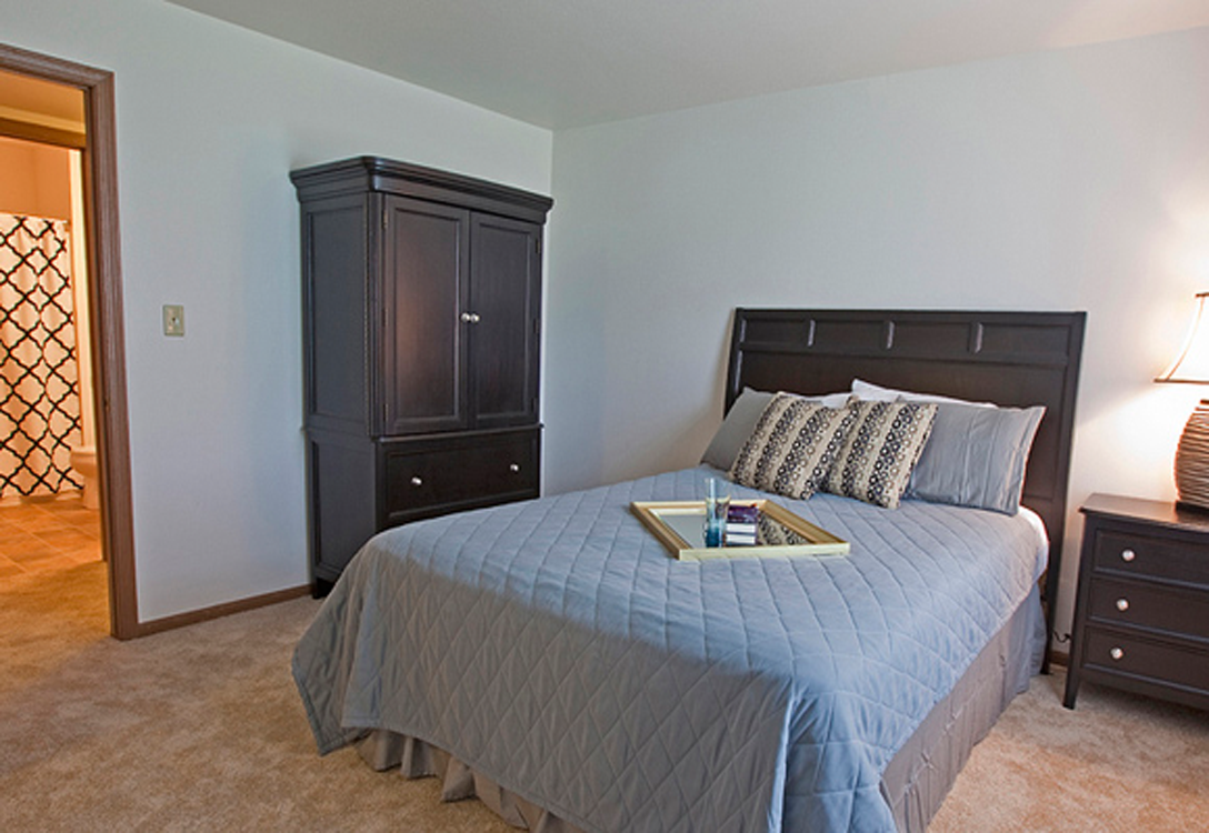 a bedroom with a bed and a dresser and a door to a bathroom