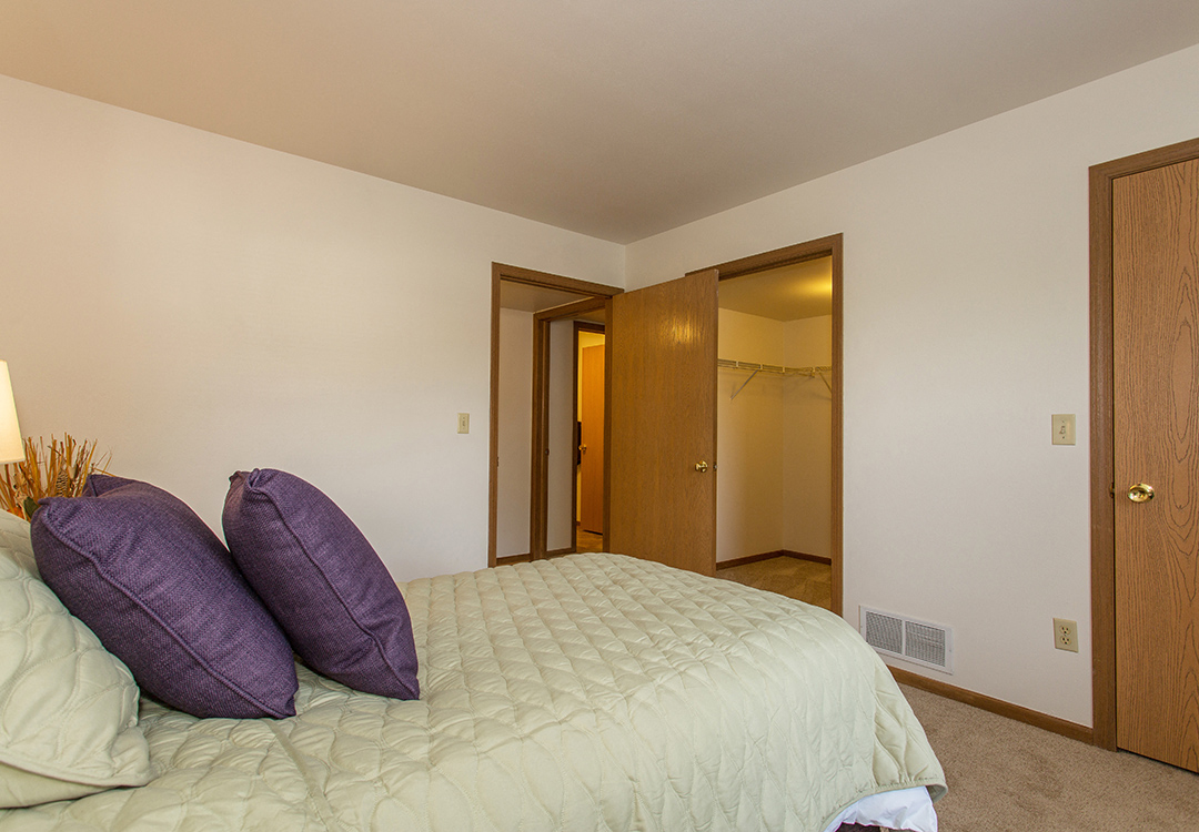 a bedroom with a bed with two purple pillows    and a closet
