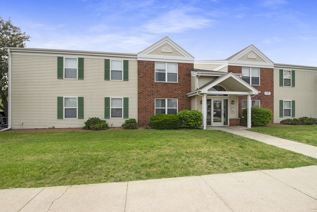 the front of an apartment building with a lawn and a sidewalk
