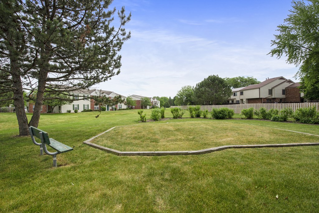 a park with a bench in the grass and a tree