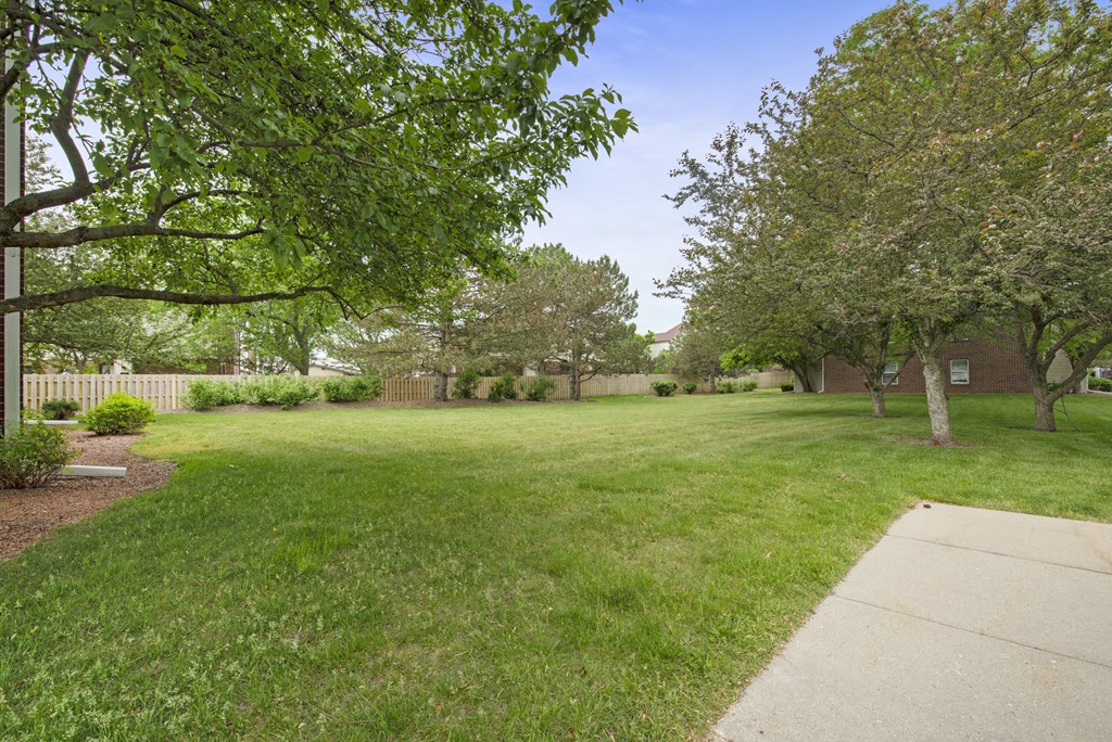 a yard with green grass and trees and a white fence