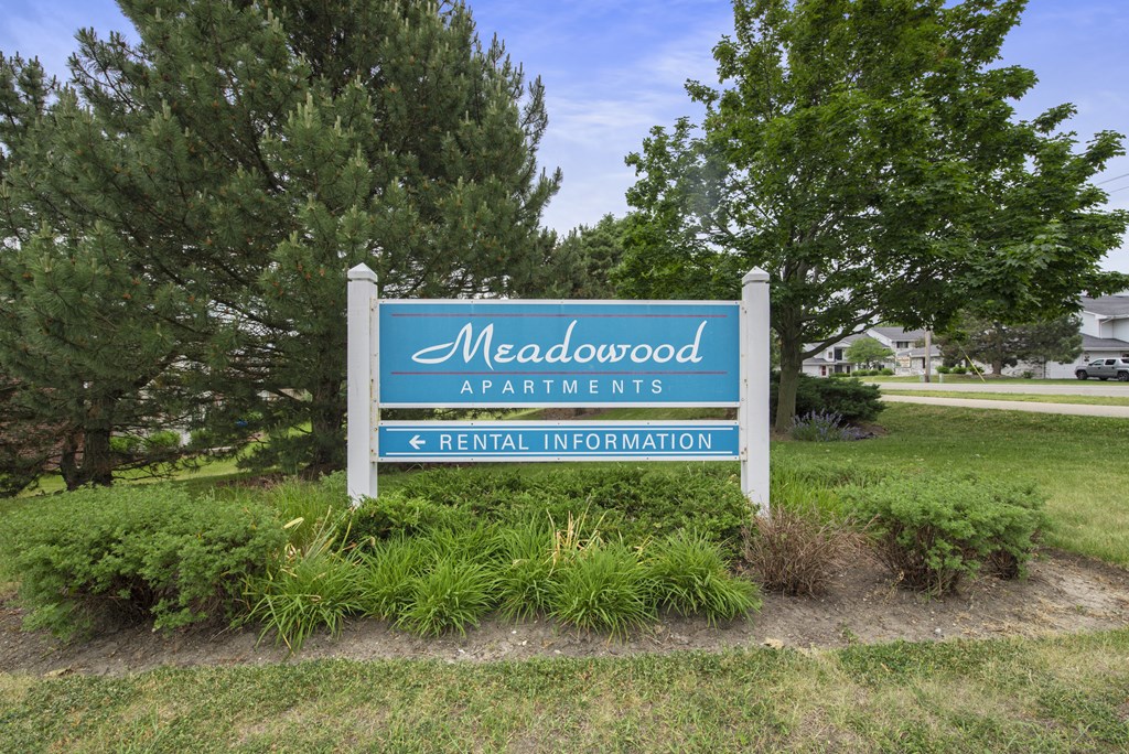 a sign for meadow apartments in front of trees
