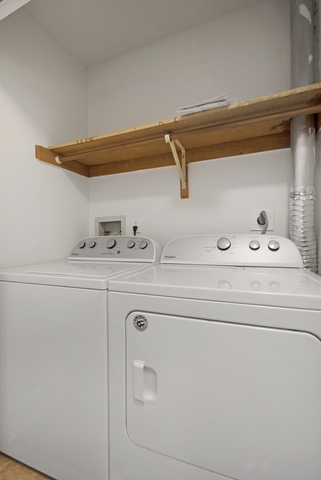 a white washer and dryer in a white room with a wooden shelf above