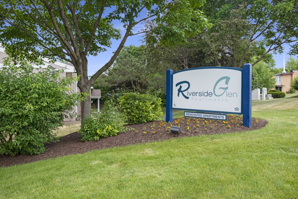 a blue and white sign in front of a yard with a tree
