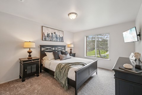 A bedroom with a bed, nightstands, and a window overlooking a green area.