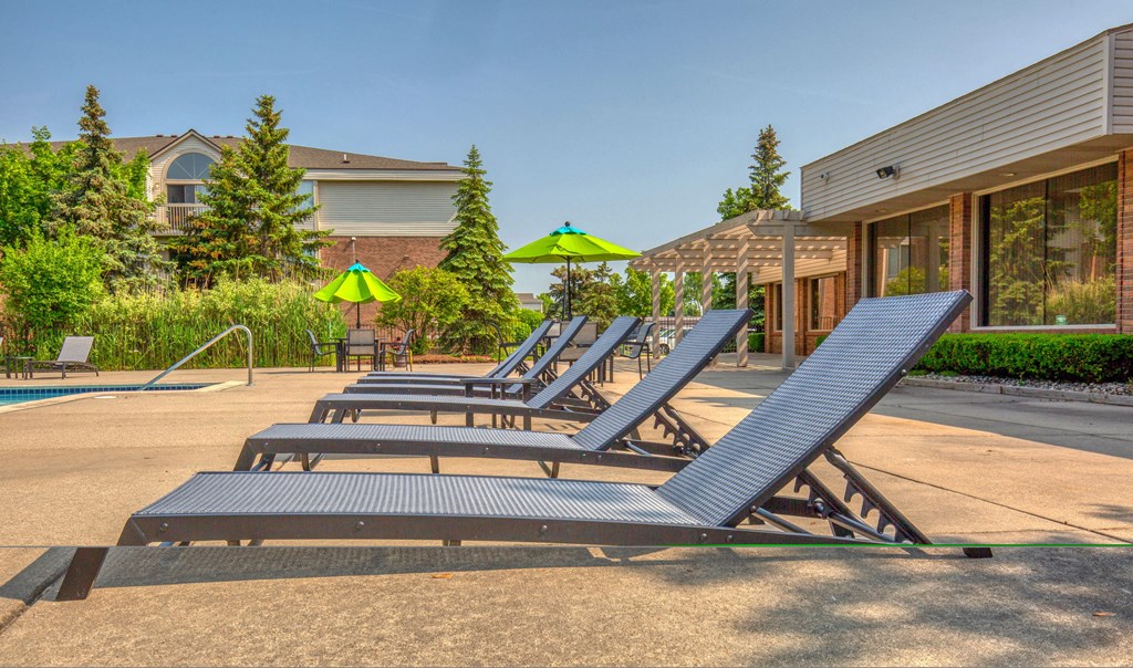 several lounge chairs in front of a pool with umbrellas at Prentiss Pointe Apartments, Harrison Township, 48045