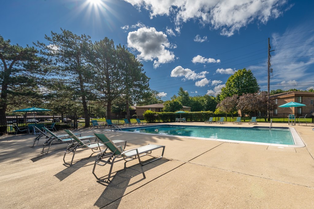 A Heated pool equipped with comfy lounge chairs at Westwood Village Apartments in Westland, MIday at the pool with lounge chairs and trees in the background.