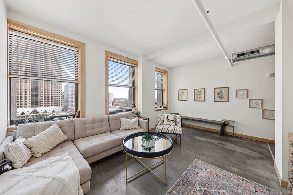 A living room with a grey sofa, a coffee table, and a large window with a view of the city.