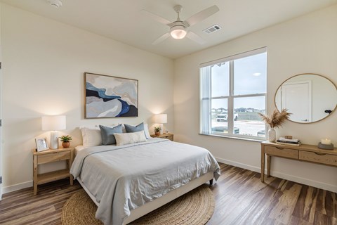 A bedroom with a large bed, a painting on the wall, and a round mirror on the dresser.