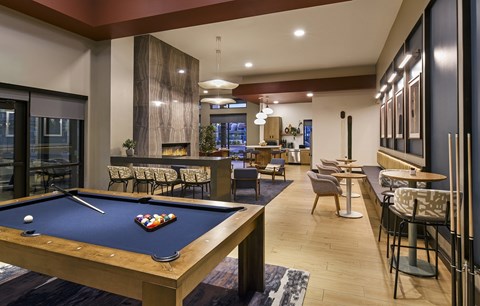 A pool table is in the middle of a room with a bar and chairs.