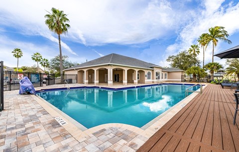 A large outdoor swimming pool with a wooden deck and a house in the background.