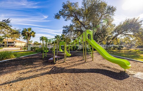 A playground with a green slide and a brown ground.