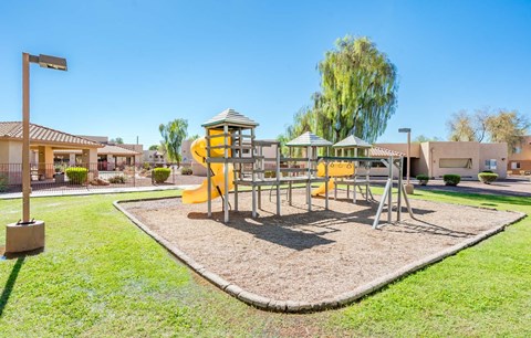 A playground with a yellow slide and a green lawn.