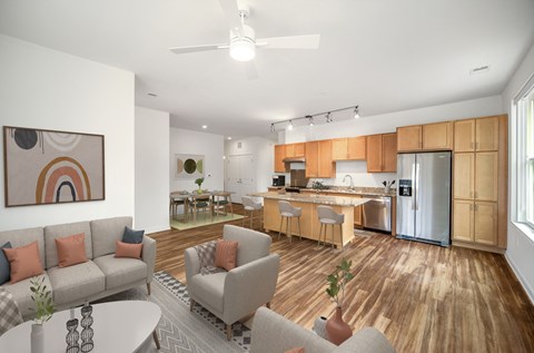 A modern living room with a grey sofa, a grey armchair, a wooden floor, and a kitchen in the background.