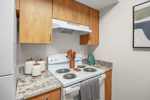 A kitchen with a white stove top oven and wooden cabinets.
