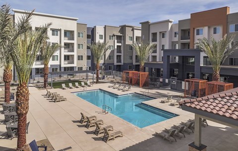 A pool surrounded by palm trees and chairs in front of apartment buildings.