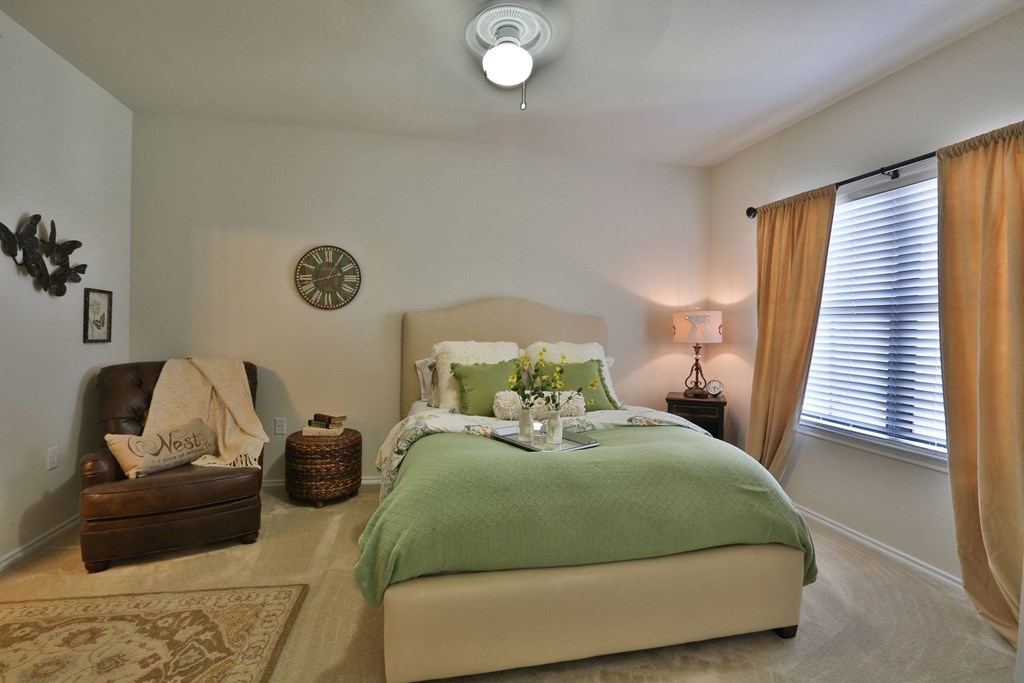 a bedroom with a bed and a chair and a clock on the wall at Cedars of Elk Drive 55+ Apartments, Burleson Texas