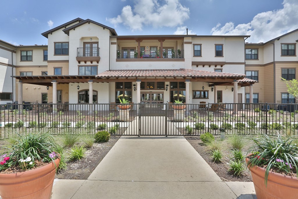 a building with a walkway and a gate in front of it at Cedars of Elk Drive 55+ Apartments, Burleson, 76028
