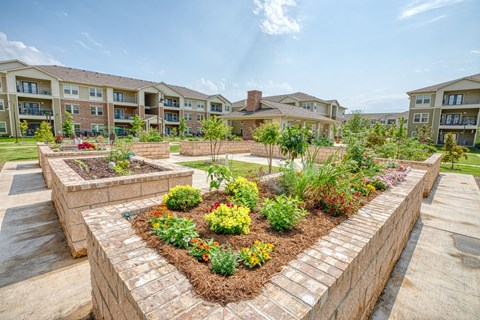 an aerial view of a community garden with apartments in the background at Sylvia at South Broadway 55+ Apartments, Joshua Texas
