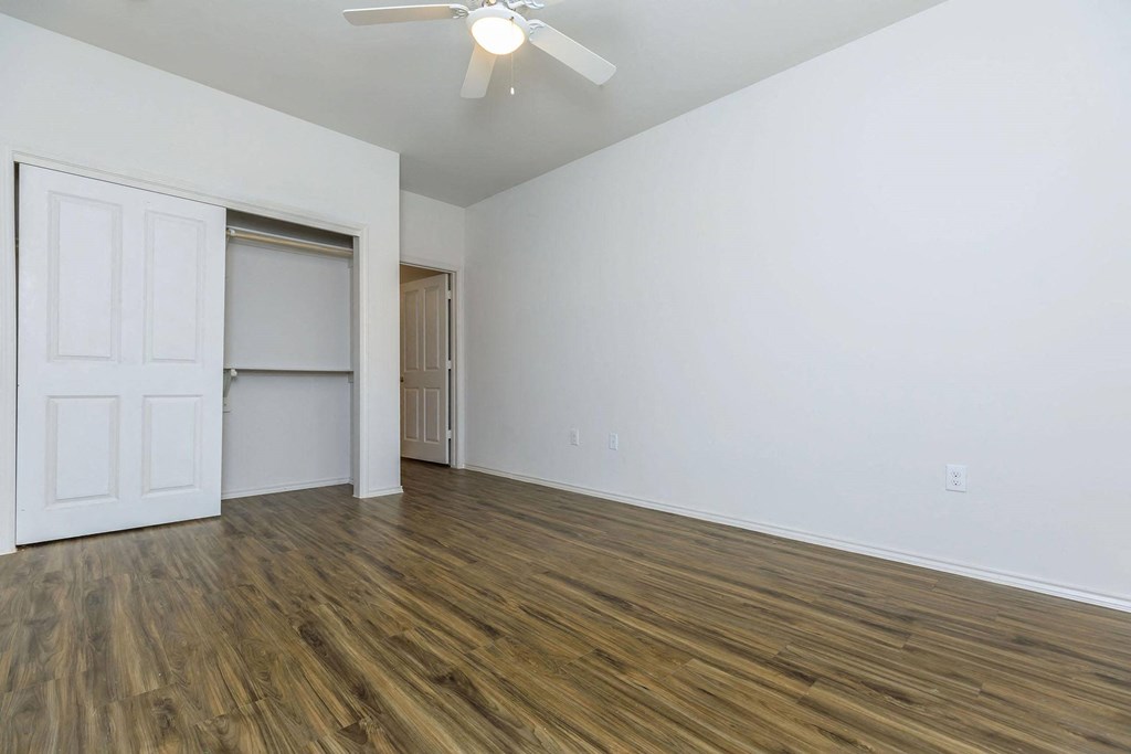 a bedroom with white walls and wood flooring and a closet at Mariposa at Westchester, Grand Prairie, TX