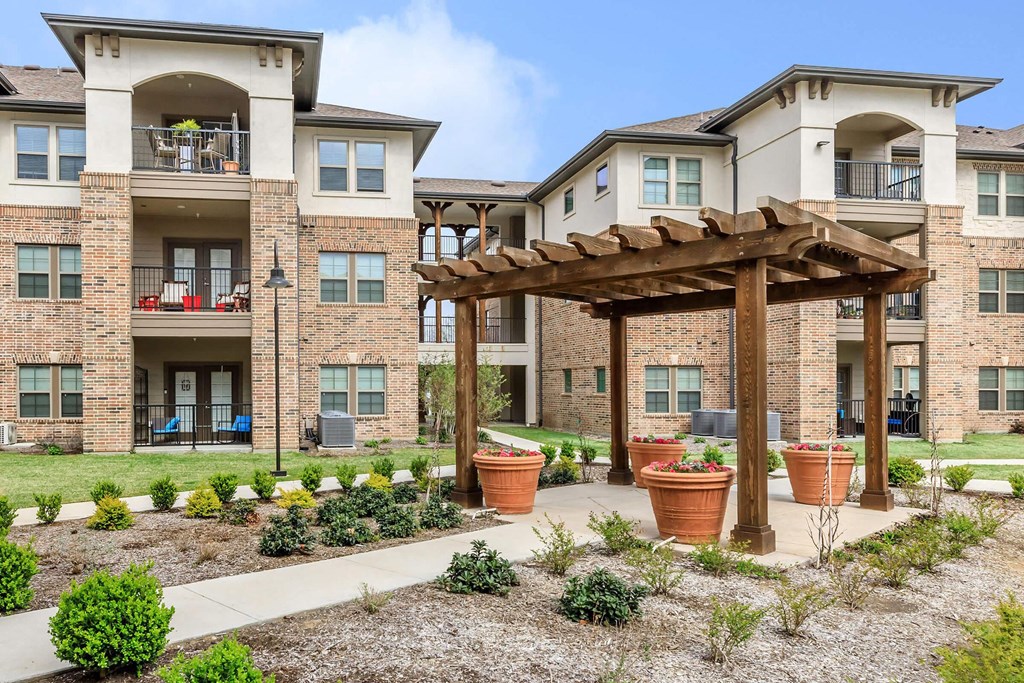 an outdoor area with potted plants in front of an apartment building at Mariposa at Westchester, Grand Prairie, 75052