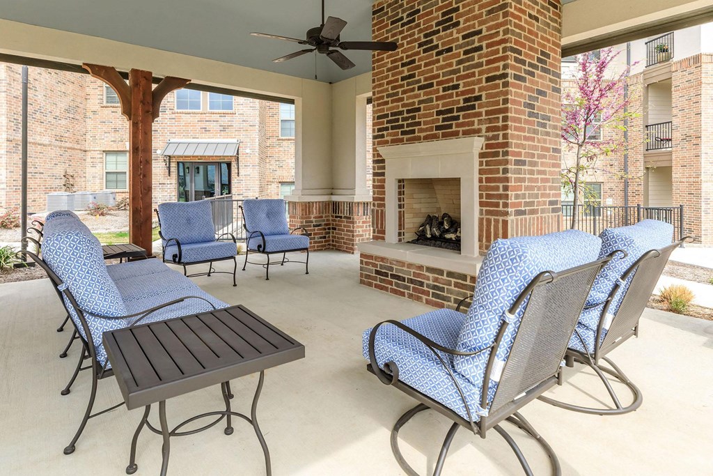 a covered patio with blue chairs and a brick fireplace at Mariposa at Westchester, Grand Prairie, TX