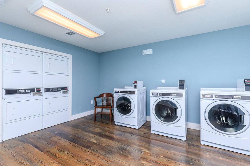 a laundry room with four washing machines and a chair at Mariposa at Westchester, Texas, 75052