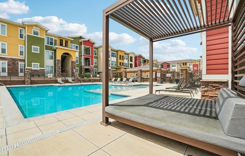A pool area with a sun lounger and a building in the background.