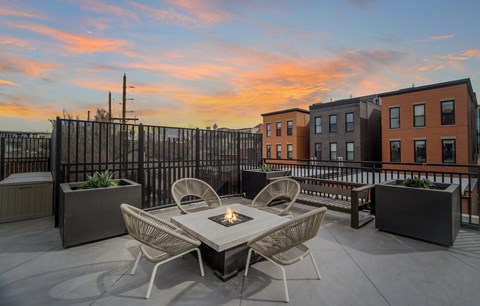 A table with chairs and a fire pit on a rooftop patio.