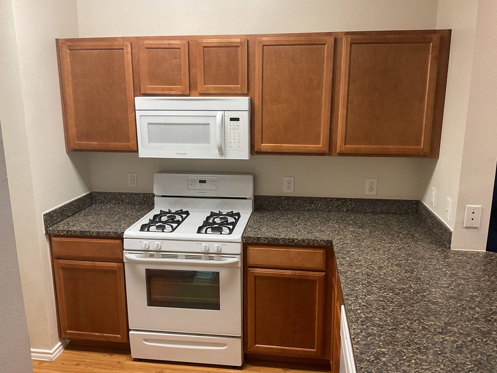 an empty kitchen with white appliances and wooden cabinets at Pacana Park 55+ Apartments, La Porte, TX