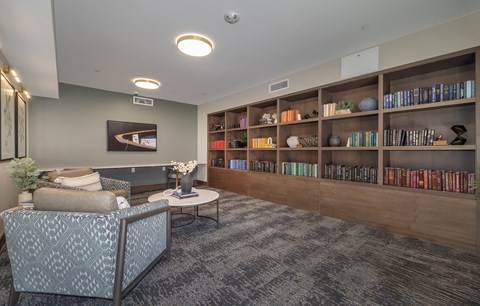 A living room with a grey patterned chair and a coffee table in front of a bookshelf.