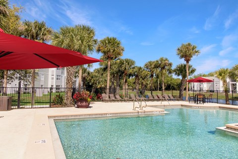 A pool surrounded by palm trees and a red umbrella.