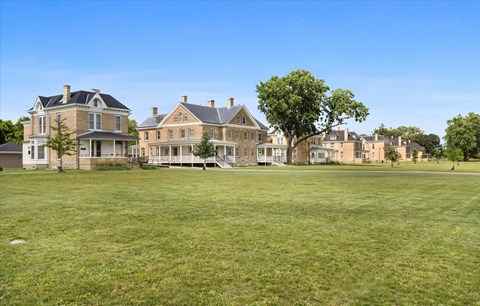 A large grassy field with a row of houses in the background.